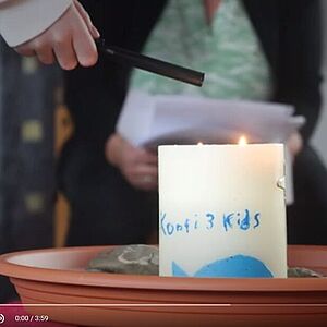 Eine Kerze mit der Aufschrift Konfi3 Kids wird angezündet